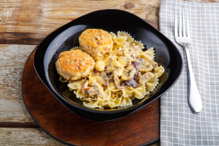 Pasta in a creamy sauce with mushrooms and chicken meatballs in a black plate on a napkin next to a fork.の写真素材