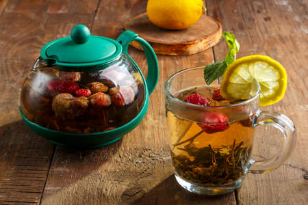 green tea in a glass cup with strawberries mint and lemon on a wooden table and a teapot and lemon in a plate and mint leaves.の写真素材