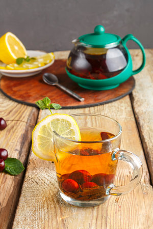 black tea in a glass cup with mint cherries and lemon on a wooden table and a teapot and lemon in a plate and mint leaves.の写真素材
