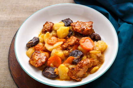 Jewish cuisine dish sweet tsimes with carrots, dates and turkey meat in a white plate on a round board on a linen background.の写真素材