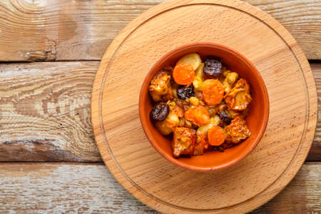A dish of Jewish cuisine tsimes with carrots, dates and turkey meat in a clay plate on a wooden round stand top view.の写真素材