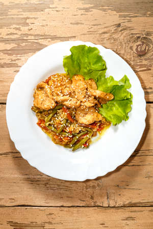 Vegetables with rice and chicken in Pan-Asian sauce and sesame seeds on salad leaves on a wooden table in a plate.の写真素材