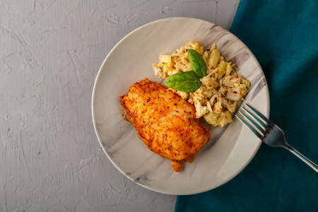 Baked chicken breast with salad on a plate decorated with spinach next to a fork on a gray background on a blue napkin stand.の写真素材