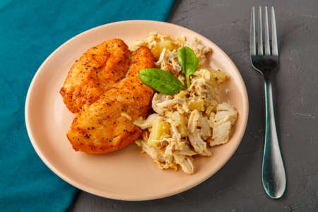 Baked chicken breast with salad on a plate decorated with spinach next to a fork on a concrete background on a blue napkin stand. Horizontal photoの写真素材