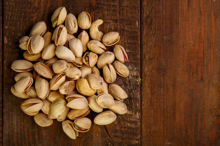Pistachio nuts are sprinkled on a dark wooden table.の写真素材
