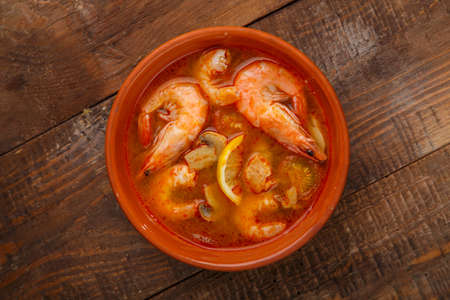 Tom yam soup with shrimps in a plate on a wooden table.の写真素材