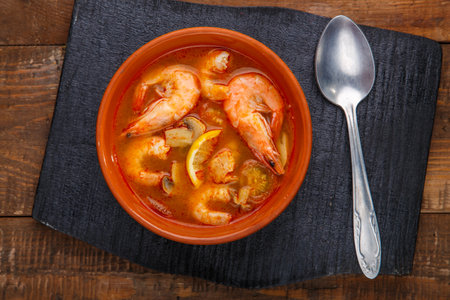 Tom yam soup with shrimps in a plate on a black stand on a wooden table.の写真素材