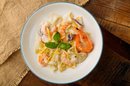 Farfalle pasta with shrimps in a creamy sauce on a gray plate on a wooden table on a linen napkin.の写真素材