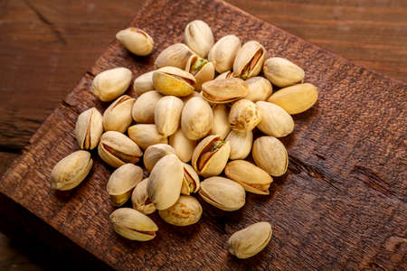 Pistachio nuts scattered on a square board on a wooden table.の写真素材