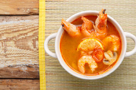 Tom yam soup with shrimps in a tureen on a mat on a wooden table.の写真素材