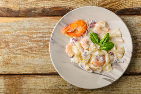 Pasta with shrimps in a creamy sauce, garnished with spinach on a gray plate on a wooden tableの写真素材