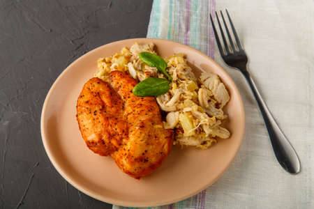 Baked chicken breast with salad on a plate decorated with spinach next to a fork on a concrete background on a gray napkin.の写真素材