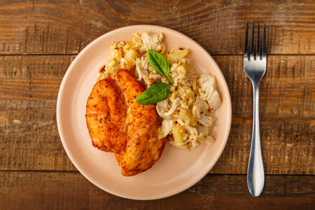 Baked chicken breast with salad on a plate next to a fork on a wooden table.の写真素材