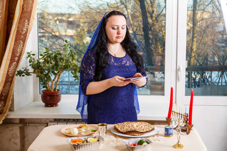 A brunette Jewish woman with her head covered in a blue cape at the Passover Seder table is reading the Passover Haggadah.の写真素材