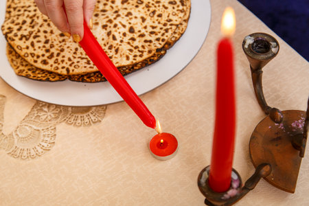 A womans hand holds a candle for the Passover Seder and lights it from a burning fire.