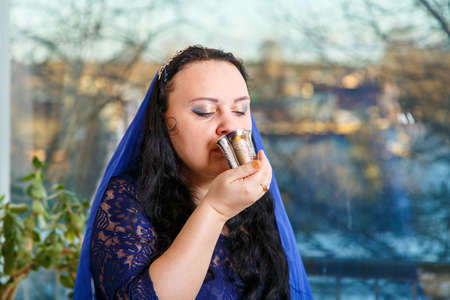 A Jewish woman with her head covered in a blue cape at the Passover Seder table drinks Kiddush wine.の写真素材