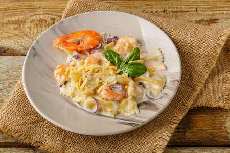 Farfalle pasta with shrimps in a creamy sauce on a gray plate on a wooden table on a linen napkin.の写真素材