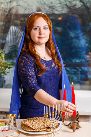 A Jewish woman with her head covered in a blue cape lights candles at a Passover Eve table.の写真素材