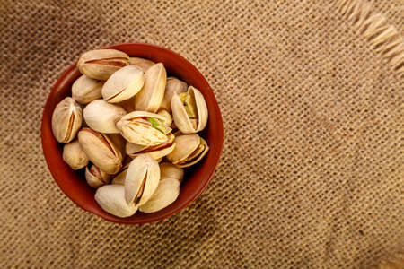 Pistachio nuts in a clay cup on burlap on a wooden table.の写真素材