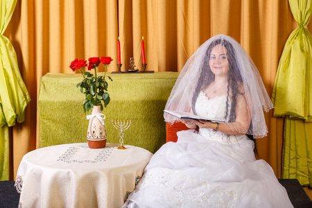 Jewish bride in white dress veiled face sits reading Tegilim before the chupa ceremony.の写真素材
