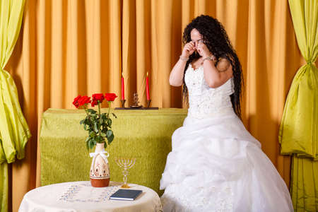 A Jewish bride in a wedding dress with her hair down in the hall is crying her groom left her before the chuppah ceremony.の写真素材