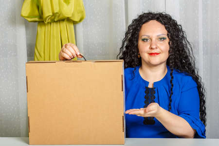Curly joyful brunette woman sits at a table in the office holding a copy of a place purchase in her hands.の写真素材