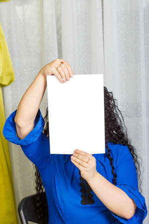 Curly joyful brunette woman sits at the table holding a copy space plate in her hands.の写真素材