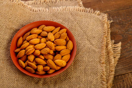 Almond nuts in a clay plate on burlap on a wooden table.の写真素材