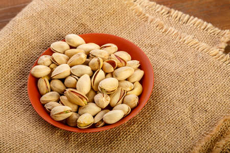 Pistachio nuts in a clay plate on burlap on a wooden table.の写真素材