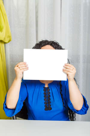 Curly joyful brunette woman sits at the table holding a copy space plate in her hands.の写真素材