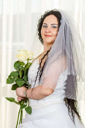 A Jewish bride stands in the hall before the chuppa ceremony with a bouquet of white roses in her hands, a photo to the waist.の写真素材