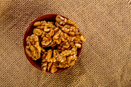 Walnuts in a clay cup on burlap on a wooden table.の写真素材