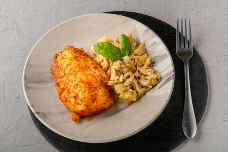 Baked chicken breast with salad on a plate decorated with spinach next to a fork on a gray background on a round black stand.の写真素材