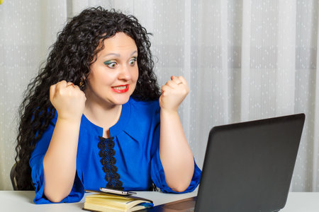 Curly brunette woman sits at a table in the office emotionally communicates via video communication.の写真素材