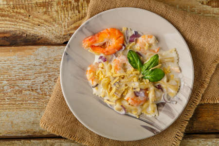 Farfalle pasta with shrimps in a creamy sauce on a gray plate on a wooden table on a linen napkin.の写真素材