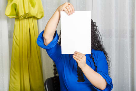 Curly joyful brunette woman sits at the table holding a copy space plate in her hands.