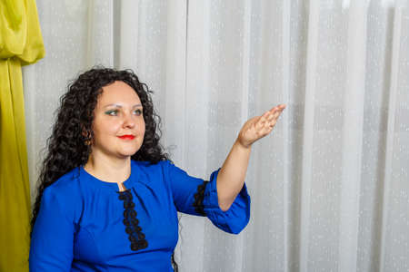 Curly-haired brunette woman in blue points to something with her hand and talks about it.の写真素材