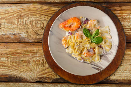Pasta with shrimps in a creamy sauce on a gray plate on a wooden tableの写真素材