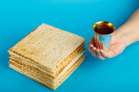 Plates of matzo laid on top of each other on a blue background and a glass of kiddush wine in hand.の写真素材