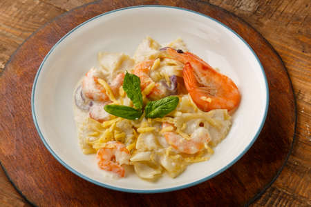 Pasta with shrimps in a creamy sauce, garnished with spinach on a gray plate on a wooden table on a round stand.の写真素材