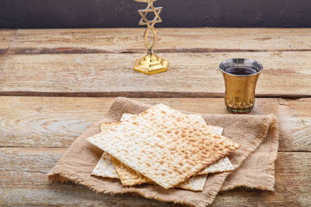 There is a candlestick on a round wooden board and a glass of kiddush wine next to the table.