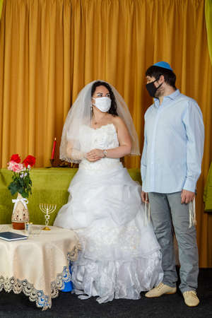 During the chupa ceremony in the synagogue, the masked Jewish bride and groom stand side by side.の写真素材