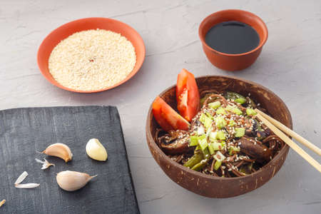 Soba with mushrooms and sesame seeds in a plate of coconut shells on a gray concrete background near garlic and soy sauce and sticks.の写真素材
