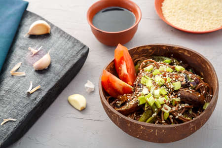 Soba with mushrooms and sesame seeds in a plate of coconut skrlup on a gray concrete background next to garlic and soy sauce.の写真素材