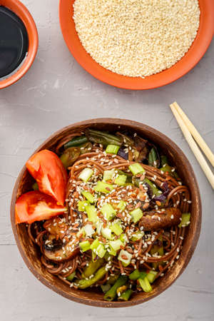 Soba with mushrooms and sesame seeds in a bowl of coconut shells on a concrete background next to sesame seeds and soy sauce and sticks.の写真素材
