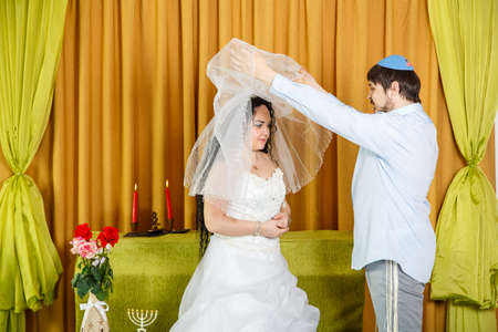 During the chuppah ceremony at a synagogue wedding, the groom lifts the veil from the brides face.の素材 [FY310167650149]