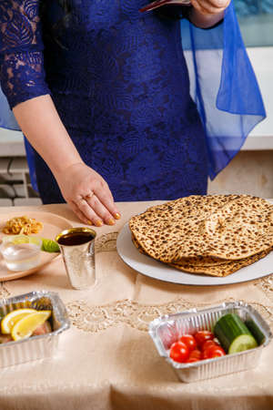 A Jewish woman with her head covered in a blue cape at the Passover Seder table breaks the matzoh shmura. Vertical photoの写真素材