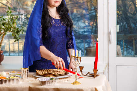 A Jewish woman with her head covered in a blue cape at the Passover Seder table breaks the matzoh shmura. Vertical photoの写真素材