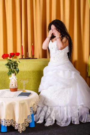 A Jewish bride in a wedding dress with a veil stands in the hall crying her groom left her before the chupa ceremony. Vertical photoの写真素材