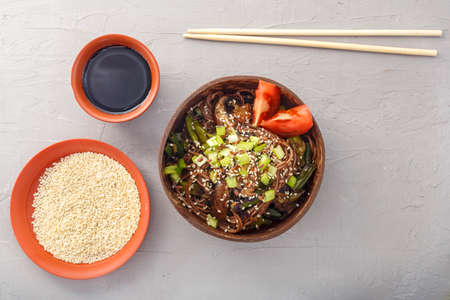 Soba with mushrooms and sesame seeds in a bowl of coconut shells on a concrete background next to sesame seeds and soy sauce and sticks. Horizontal photoの写真素材